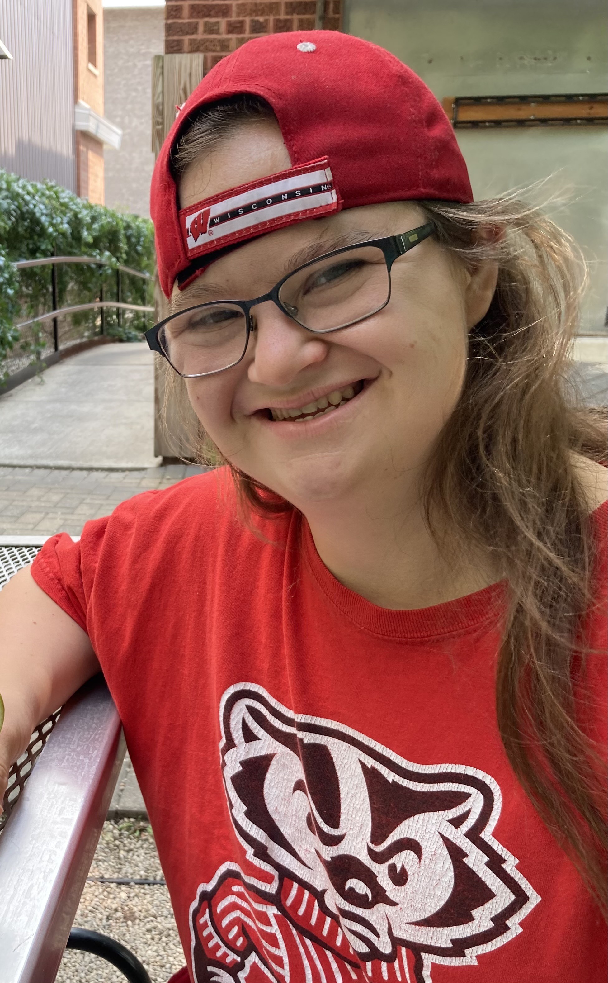 A white woman in a red hat and T-shirt, wearing black-framed glasses smiling into the camera
