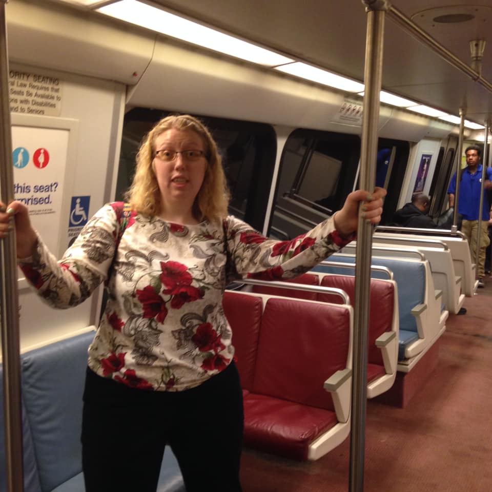 a white woman wearing a floral shirt is standing in the subway holding on to railings