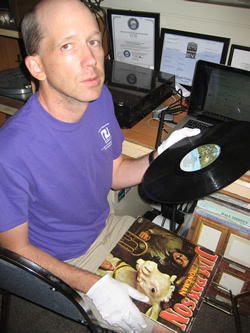 Brian, wearing white protective gloves and looking up at the camera, sits with a Jim Dawson record in his left hand and the record cover on his lap.