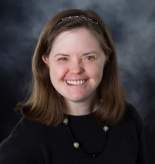 A portrait-style headshot of Mia smiling against a blue-gray background